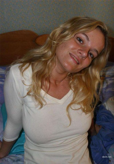 Кудрявая блондинка стягивает с себя одежду, соблазняя взглядом